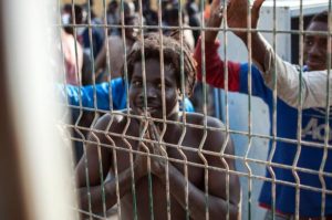 An-illegal-migrant-gestures-behind-a-fence-at-the-Centre-for-Temporary-Stay-of-Immigrants