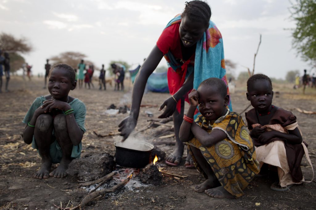 A woman cooks a meal outside in the open air with her three children where she is camping with her family the night before being able to register for a ration card  in Thanyang, South Sudan on March 20, 2016. Nearly 15,000 people from surrounding areas made their way to Thanyang to register for support with Unicef  and the WFP who are running a Rapid Response Mission to support the most in accessible regions affected by the ongoing civil war.  There are no health clinics, bore holes, schools or roads in the area and some people walked for two days to get there. The only water people have access to comes from the swamp. During the Rapid Response Mission (RRM) in Thanyang, Unity State that took place on 18-24 March, WFP and UNICEF teams has provided assistance to nearly 15,000 people. This included providing 1,243 children with OPV vaccine, screening 2,820 children for malnutrition and registering 27 severely malnourished and 357 moderately malnourished children; setting up two new classrooms and registering 900 children for school, setting up a child friendly space for some 730 children and registering 27 separated and 5 missing children. Rapid Response Mechanism (RRM) provides life-saving assistance to children and families affected by conflict, targeting hard-to-reach locations where partners are unable to adequately respond to the immense levels of need. In addition to providing immediate services, the RRM establishes a framework of humanitarian access, which enables partners to establish longer  term presence in disaster  affected locations. Through the RRM, UNICEF provides critical multi-sector emergency response including: health, child protection, education, nutrition and WASH.