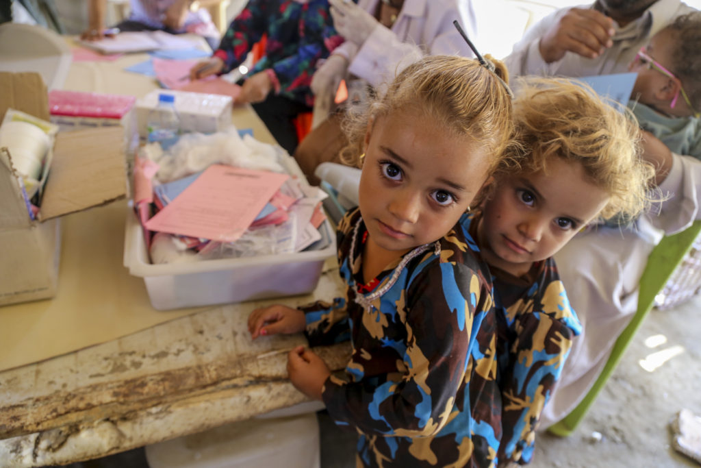 On 15 July, two girls wait in line at a temporary medical centre in Bzebiz Displacement Camp in Baghdad Governorate. With support from UNICEF, WHO, and the Ministry of Health, the medical convoy provided vaccinations and health and nutrition support to vulnerable displaced children in this and other camps in the area. With support from the Ministry of Health, WHO and UNICEF, a mobile medical convoy visits camps for internally displaced families in Baghdad Governorate in order to provide vaccination and health and nutrition support to vulnerable children living in the camps. As part of an ongoing emergency response to the humanitarian crisis in Iraq, from January 2015 through May 2016, UNICEF and partners supported the following health initiatives: Nationwide communication and social mobilization efforts for the oral cholera vaccination and polio campaigns; support to the Ministry of Health and the Directorates of Health to enhance routine immunisations for Syrian refugees and IDPs, along with strengthening health systems in under-served communities; procurement and distribution of cold chain equipment, as well as polio and measles vaccines; a 'baby-hut' initiative that provides breastfeeding counselling to pregnant and lactating women. By July 2016 in Iraq, an estimated 10 million people - including 4.7 million children, or one third of all children in Iraq - were in urgent need of humanitarian assistance, including 3.3 million internally displaced people, returnees, host communities in need, and people in areas under control by or newly liberated from armed groups, as well as 245,000 refugees from the Syrian Arab Republic.