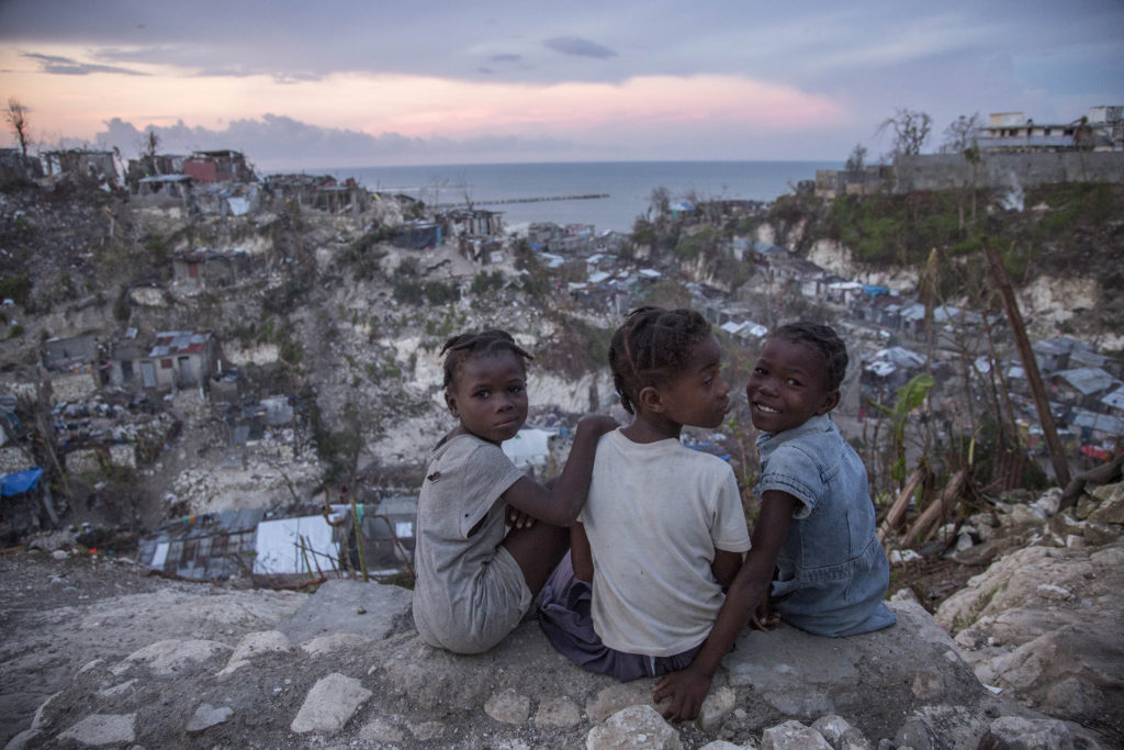 On 13 October 2016 in Jérémie, Haiti, Mylove Théogène, 8, sits with other girls near her home.  Myloves family stayed in their home on a hilltop until their home collapsed around 5:00am on the night Hurricane Matthew struck Haiti. Then, the family then moved to a school house for shelter.  "I thought I was going to die.  I thought my family would all die" said Mylove.  The family of five lost their father in February 2016, when he fell from a tree while collecting fruit for the family to eat. "When I grow up I want to go to school" Mylove remarks as a second-grader who has not been to school at all in 2016.  More than one week after Hurricane Matthew, as schools re-open across the country, more than 100,000 children will be missing out on learning after their schools were either damaged or converted into shelters. Hurricane Matthew passed over Haiti on Tuesday October 4, 2016, with heavy rains and winds. While the capital Port au Prince was mostly spared from the full strength of the class 4 hurricane, the western area of Grand Anse, however was in the direct path. The cities of Les Cayes and Jeremie received the full force sustaining wind and water damage across wide areas. Coastal towns were severely damaged as were many homes in remote mountainous regions. International relief efforts are underway to provide food water and shelter to the people affected by the storm. An estimated 500,000 children live in the Grande Anse Department and Grand South Department in southern Haiti, the areas worst hit by Hurricane Matthew.  UNICEF had prepositioned emergency supplies with national authorities to reach up to 10,000 people.  On 8 October, six water trucks arrived in Jeremie and Les Cayes, the respective capital cities within the Departments.  Additional water and sanitation supplies, such as water purification tablets, water bladders and plastic sheeting, have been dispatched to the most affected departments in the westernmost tip of Haiti.  As of 10 October, UN